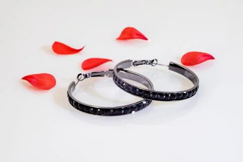 Two dark round earrings with bright black stones and red flower petals. Stock Photos