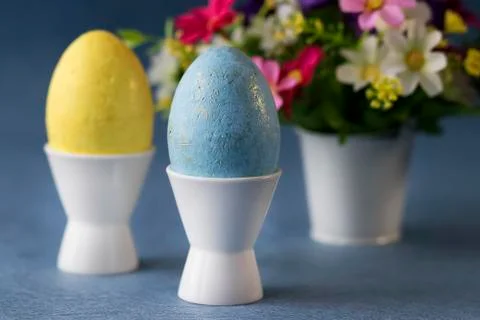 Two decorative eggs in white coasters and bright flowers on a gray background Stock Photos