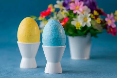 Two decorative eggs in white coasters and bright flowers on a gray background Stock Photos