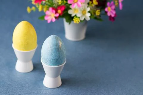 Two decorative eggs in white coasters and bright flowers on a gray background Stock Photos
