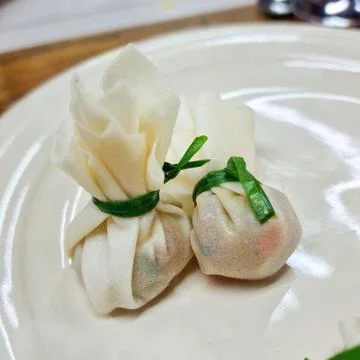Two delicate dumplings, wrapped in thin dough and tied with green chives Stock Photos