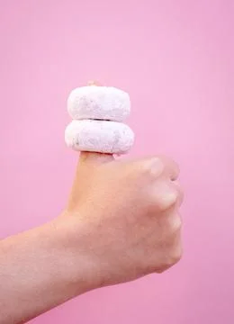 Two delicious donuts embedded in the thumb of a hand with a pink background. Stock Photos