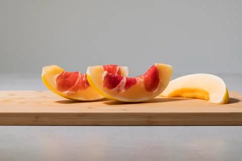 Two delicious looking melon slices with cured ham on top next to another slic Stock Photos