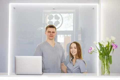 Two dentists stand at the reception in a beautiful clinic and greet patients Stock Photos