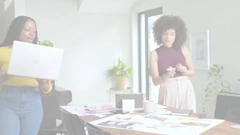 Two designers at table handing laptop, finalizing layouts while scanlines Stock Footage 333540179