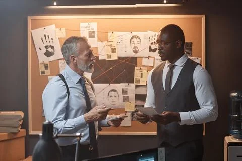 Two detectives discussing case standing by evidence board in office Stockfoto's