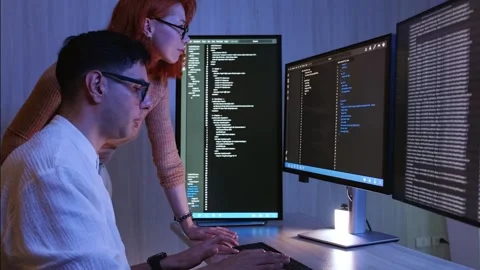 Two developers collaborate at dual monitors, reviewing code and data Stock Footage 318578703