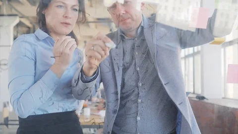 Two developers, a man and a woman, write formulas on a glass board with a marker Stock Footage 108984473