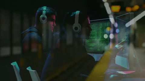 Two devs tech desk collaborating, right gesturing to green code monitors while Stock Footage 332545201