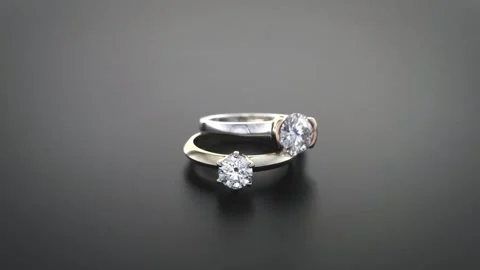 Two diamond engagement rings rotating on dark reflective background. Stock Footage 346610451