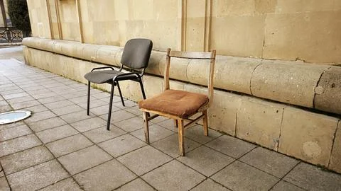 Two Different Chairs Standing Against a Stone Wall. Stock Photos