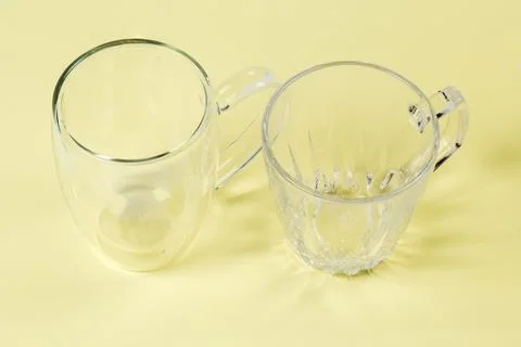Two different empty glass cups on a yellow surface Stock Photos