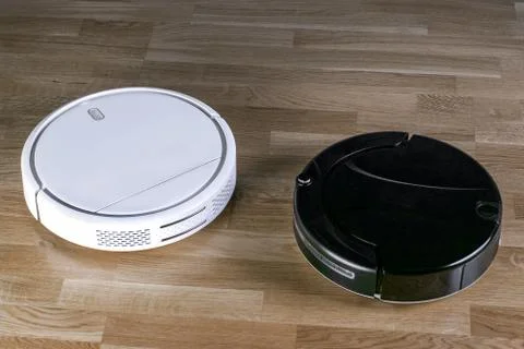 Two different robotic vacuum cleaners models cleaning dust on laminate floors Stock Photos