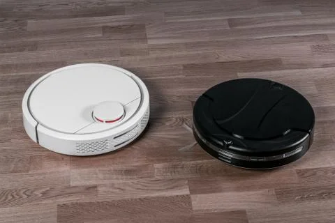 Two different Robotic vacuum cleaners on dark laminate floor, smart home robo Stock Photos