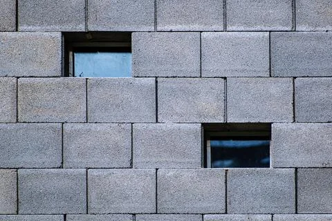 Two different small square windows on the outer wall of a cement block Stock Photos
