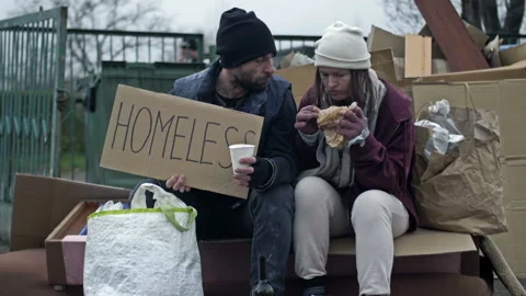 Two dirty and poorly dressed homeless people, a man and a woman, sit by a pile Stock Footage 239628871