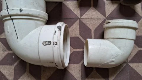 Two dirty white plastic pvc pipe elbow joints on patterned tiles Stock Photos