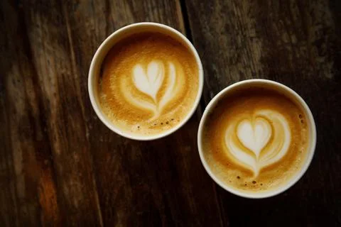 Two disposable cups of coffee with the heart on foam on a wooden table. Stock Photos