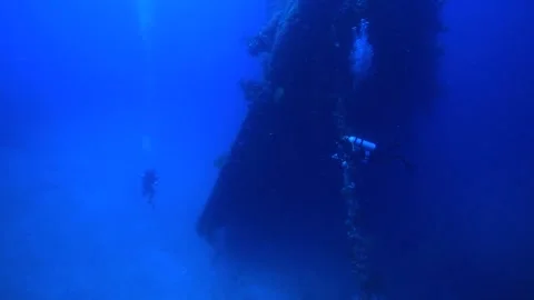 Two divers swim in front of the vast wreck of a ship. Video stock 325733463