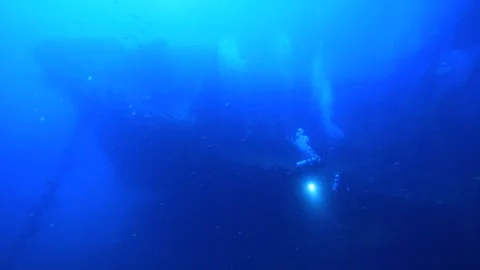 Two divers swim in front of the vast wreck of a ship. Stock Footage 325733464