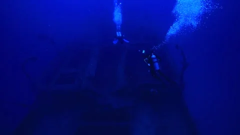 Two divers swim in front of the vast wreck of a ship. Stock Footage 325733473