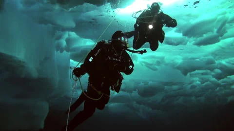 Two divers under the Arctic ice at the North Pole light the way a flashlight. Stock-Footage 62986144