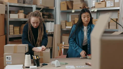 Two diverse female workers packing parcels with scotch tape while working 스톡 동영상 169339943