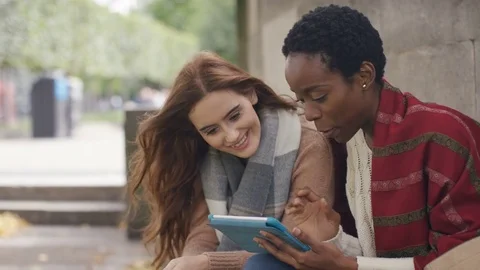 Two diverse friends outdoors talking and using a digital tablet together Stock Footage 80298477