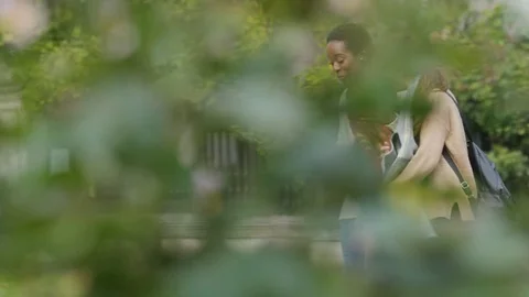 Two diverse friends walking through city gardens talking, in slow motion Video stock 80301776