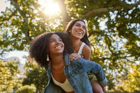Two diverse multiracial friends having fun laughing and giving a piggyback to Stock Photos