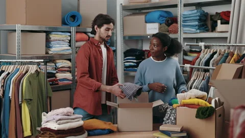 Two diverse people working at the donating center and putting clothes at the Stock Footage 226615378
