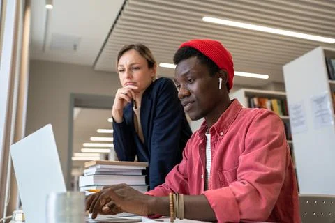 Two diverse students study partners learning together in library, using online Stock Photos