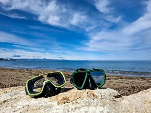 Two diving masks rest on a seaside rock with a clear blue sky and ocean wat.. Foto stock