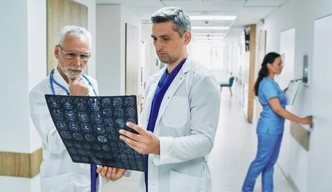 Two doctors analyzing MRI scan of patient's brain while standing in corridor  Stock Photos