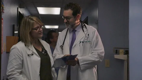 Two doctors consulting with each other while looking at a clipboard together Stock Footage 101448392