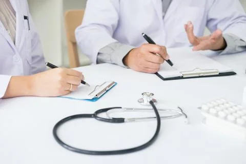Two doctors discussing patient notes in an office pointing to a clipboard wit Stock Photos