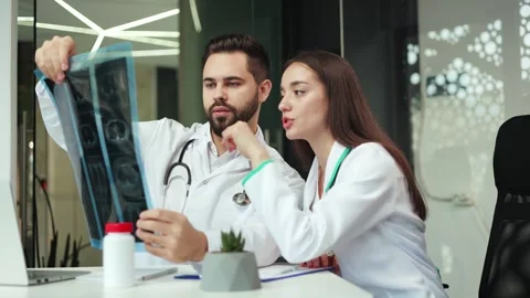Two doctors discussing results of X-ray and making notes about it at workplace Stock Footage 257940334