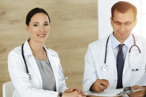 Two doctors discussing treatment problems while sitting at the desk in sunny Stock Photos