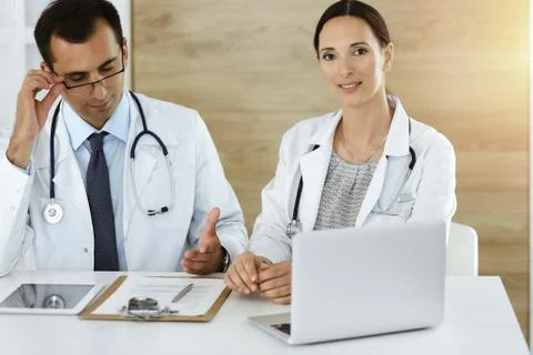 Two doctors discussing treatment problems while sitting at the desk in sunny Stock Photos