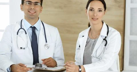 Two doctors discussing treatment problems while sitting at the desk in hospital Stock Photos