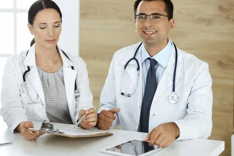 Two doctors discussing treatment problems while sitting at the desk in hospital Stock Photos