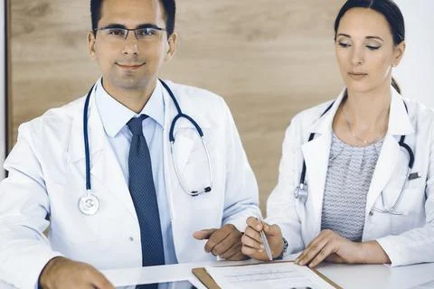 Two doctors discussing treatment problems while sitting at the desk in hospital Stock Photos