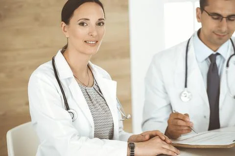 Two doctors discussing treatment problems while sitting at the desk in hospital Stock Photos
