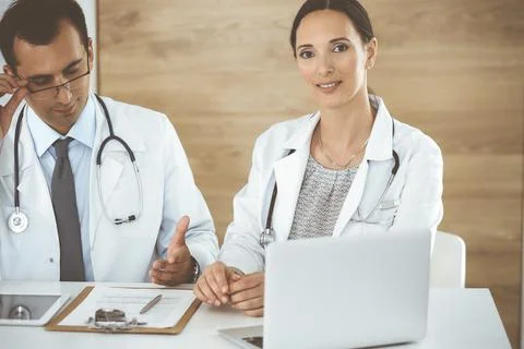 Two doctors discussing treatment problems while sitting at the desk in hospital Stock Photos