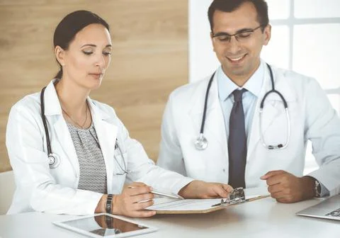 Two doctors discussing treatment problems while sitting at the desk in hospital Stock Photos
