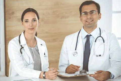 Two doctors discussing treatment problems while sitting at the desk in hospital Stock Photos
