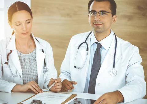 Two doctors discussing treatment problems while sitting at the desk in sunny 스톡 사진
