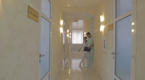 Two doctors leave the office walk down the corridor and discussing Stock Footage 61377321