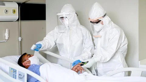 Two doctors in protective suits visiting a corona virus patient in his room Stock Footage 241739335