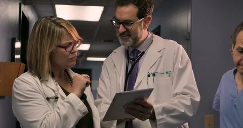 Two doctors reviewing a case on a digital tablet in a busy practice or hospital Stock Footage 102349739